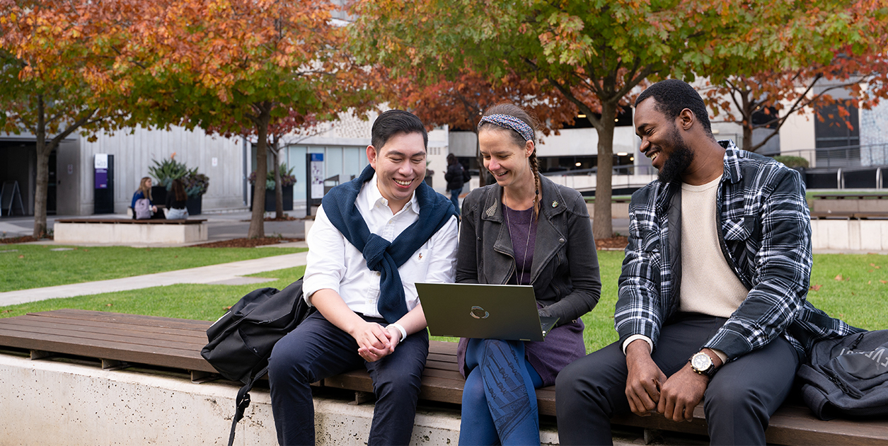 Three ACU students are sitting outside on campus chatting.