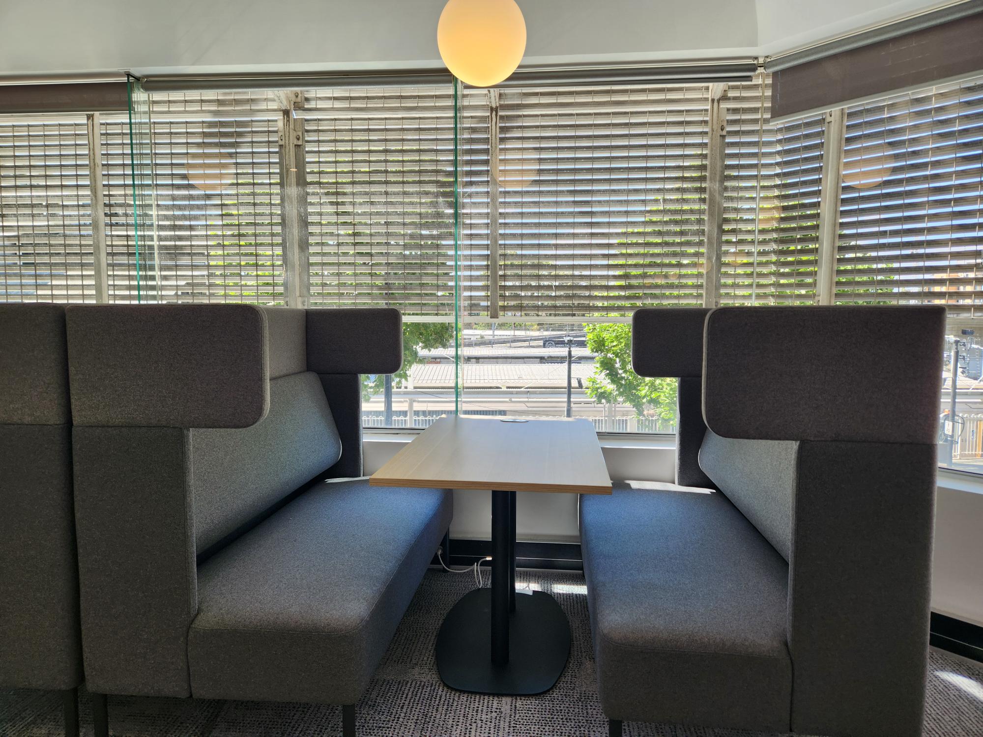Two grey booth seats with a desk between them, facing a large open window.